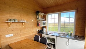 A compact kitchen with wooden walls, a dining table with chairs, a built-in sink, and a window offering a view of the outdoors.