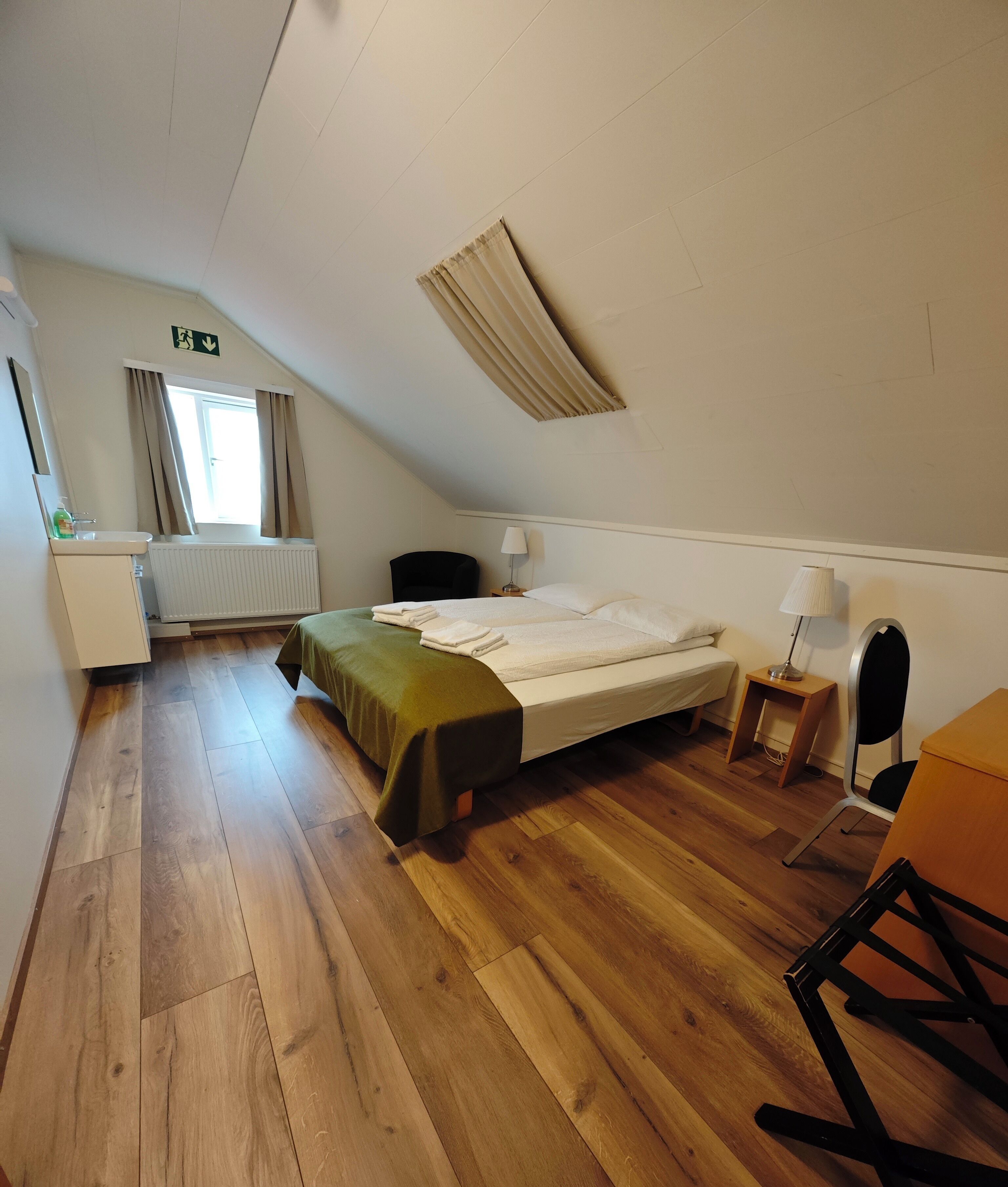 A room with a bed, a chair, a desk, a radiator, and a window with curtains.