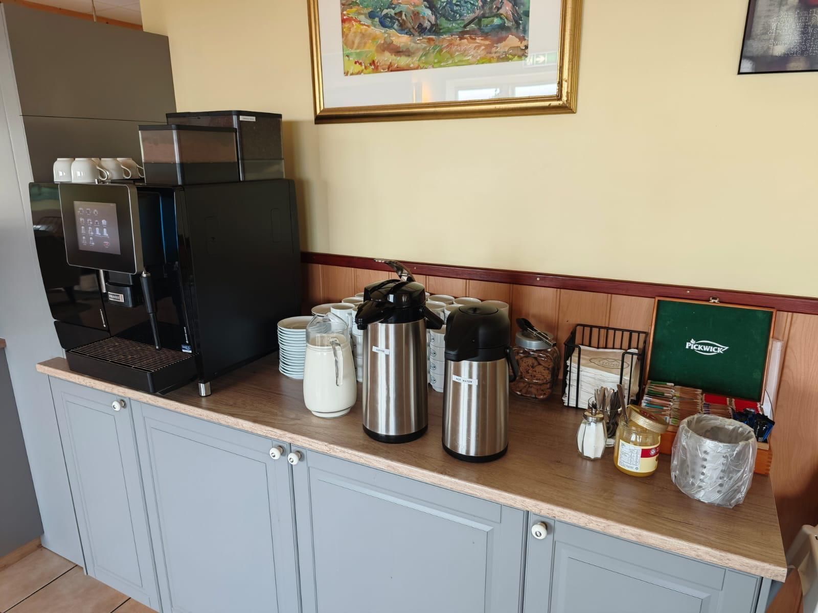 A coffee station with a coffee machine, milk jug, thermos, and condiment dispensers.