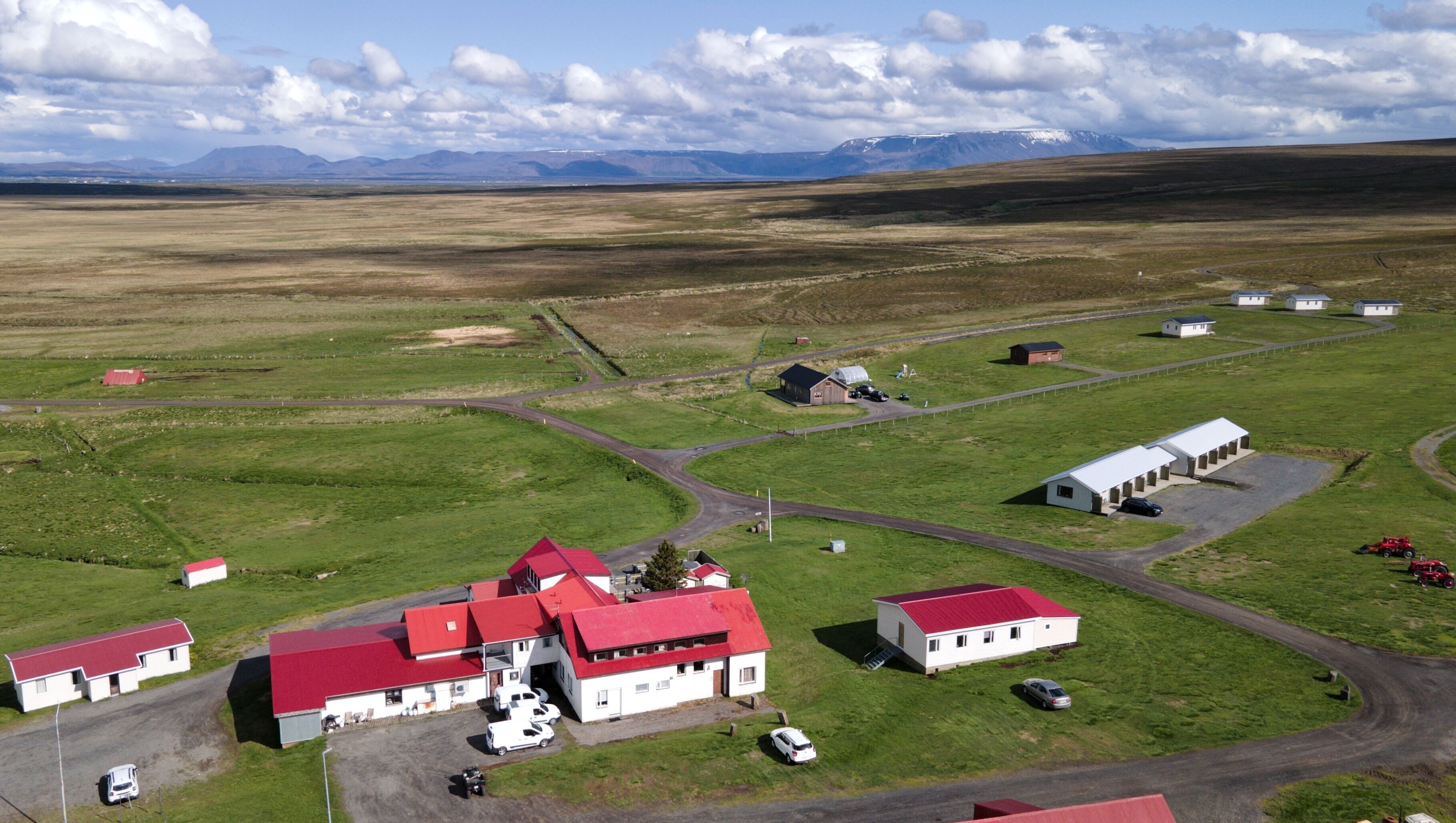 An aerial view of a rural area with several buildings, including a large white structure with a red roof, smaller white buildings, and a red barn.