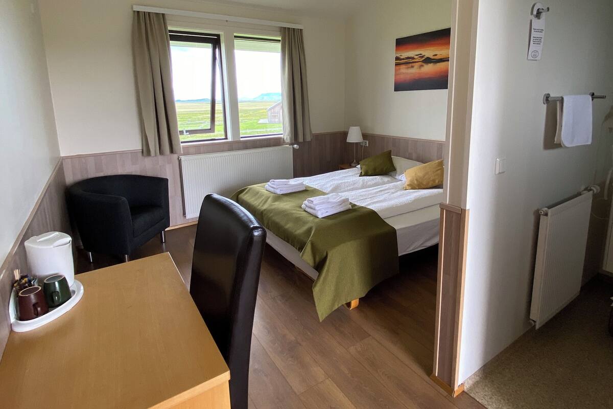 Een hotelkamer met een bed, een bureau, een stoel, een radiator en een raam met gordijnen.