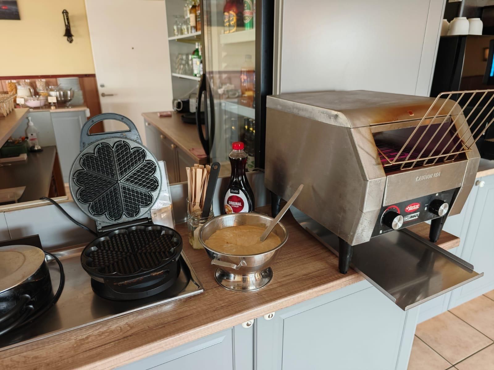 A kitchen with a waffle maker, a hot plate, a bowl with a spoon, and a hot grill.