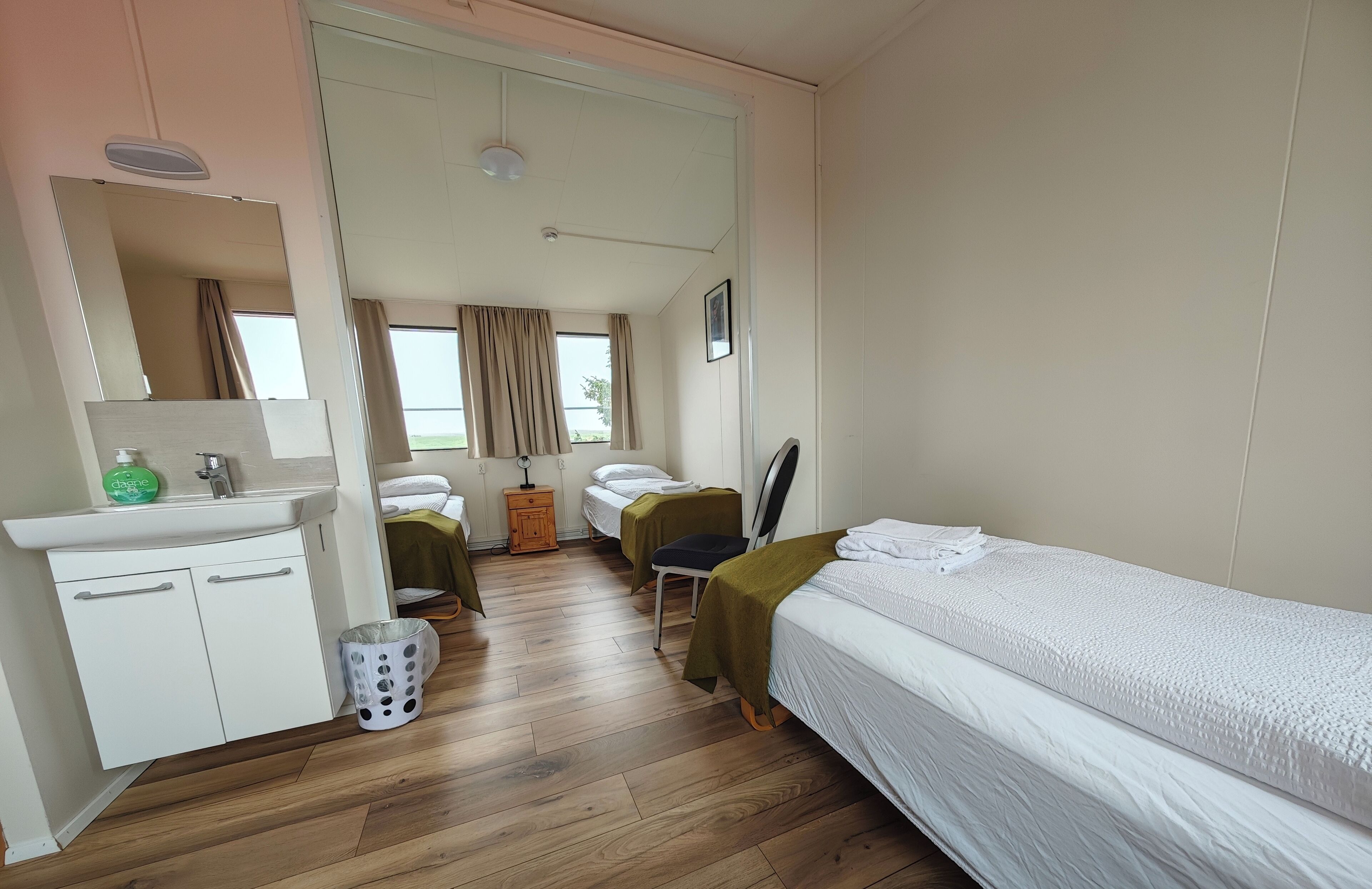 A hotel room with a bed, a desk, a chair, a mirror, a sink, and a window with curtains.