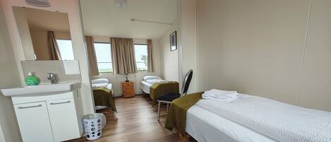 A hotel room with a bed, a desk, a chair, a mirror, a sink, and a window with curtains.