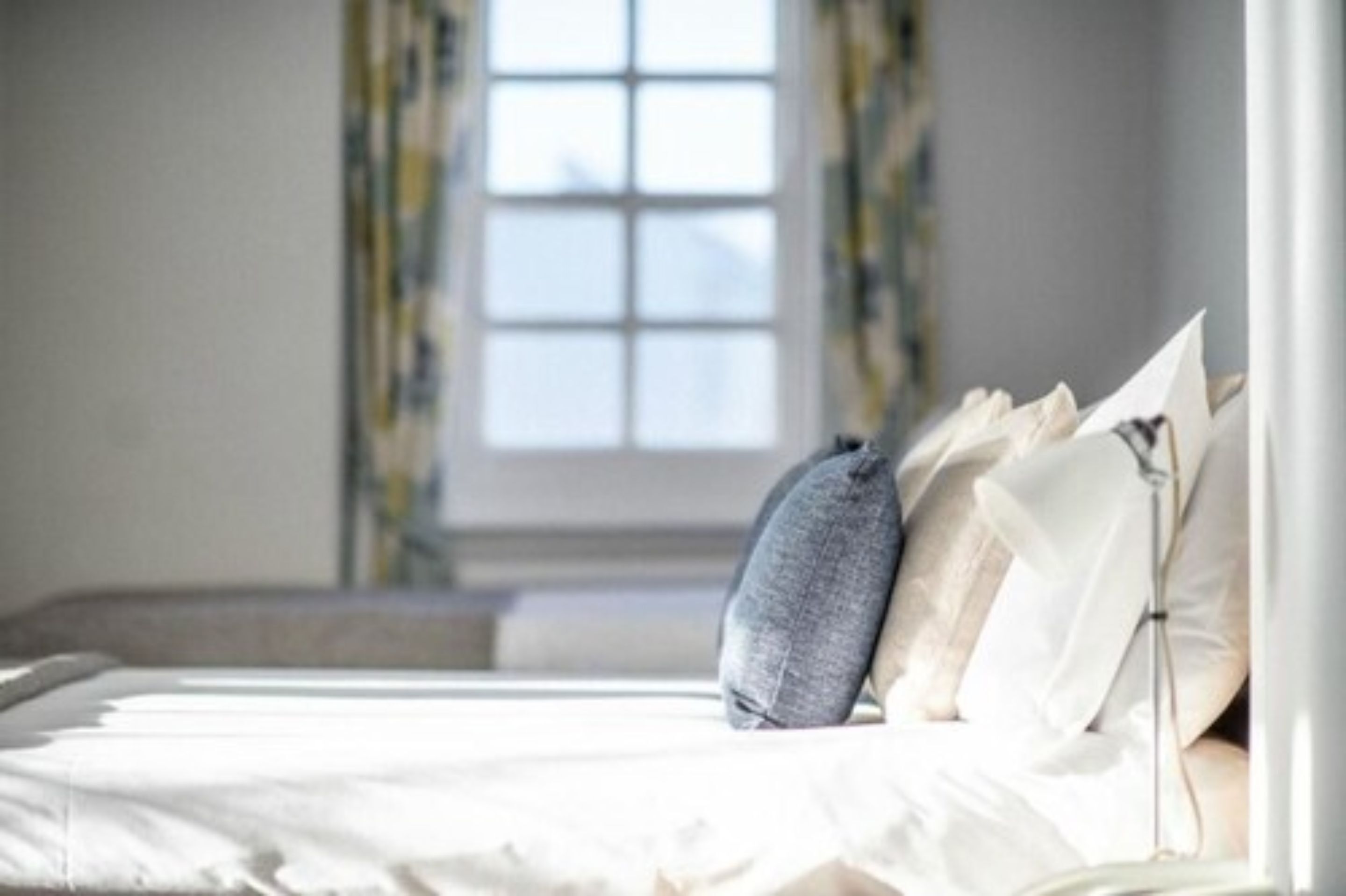 Un dormitorio con cama, almohadas y ventana con cortinas.