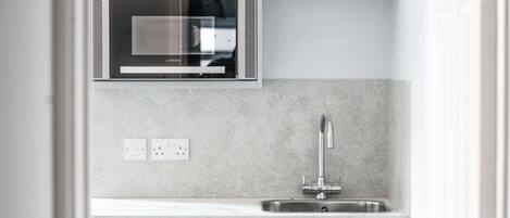 A compact kitchen with a built-in microwave, a stainless steel sink, and light grey cabinetry.