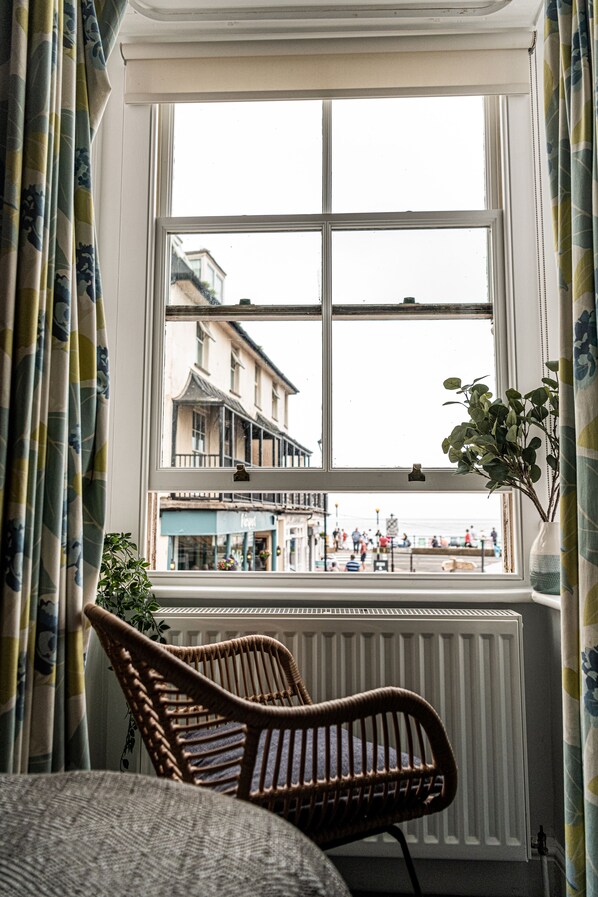 Una habitación con vista a un paseo marítimo, una silla de mimbre y una planta en maceta.