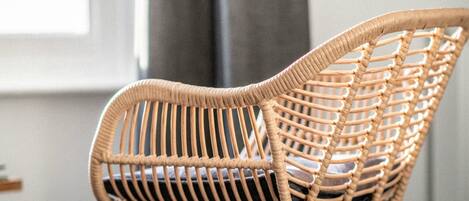 A wicker chair with a metal frame, positioned in a room with a window and a grey curtain.