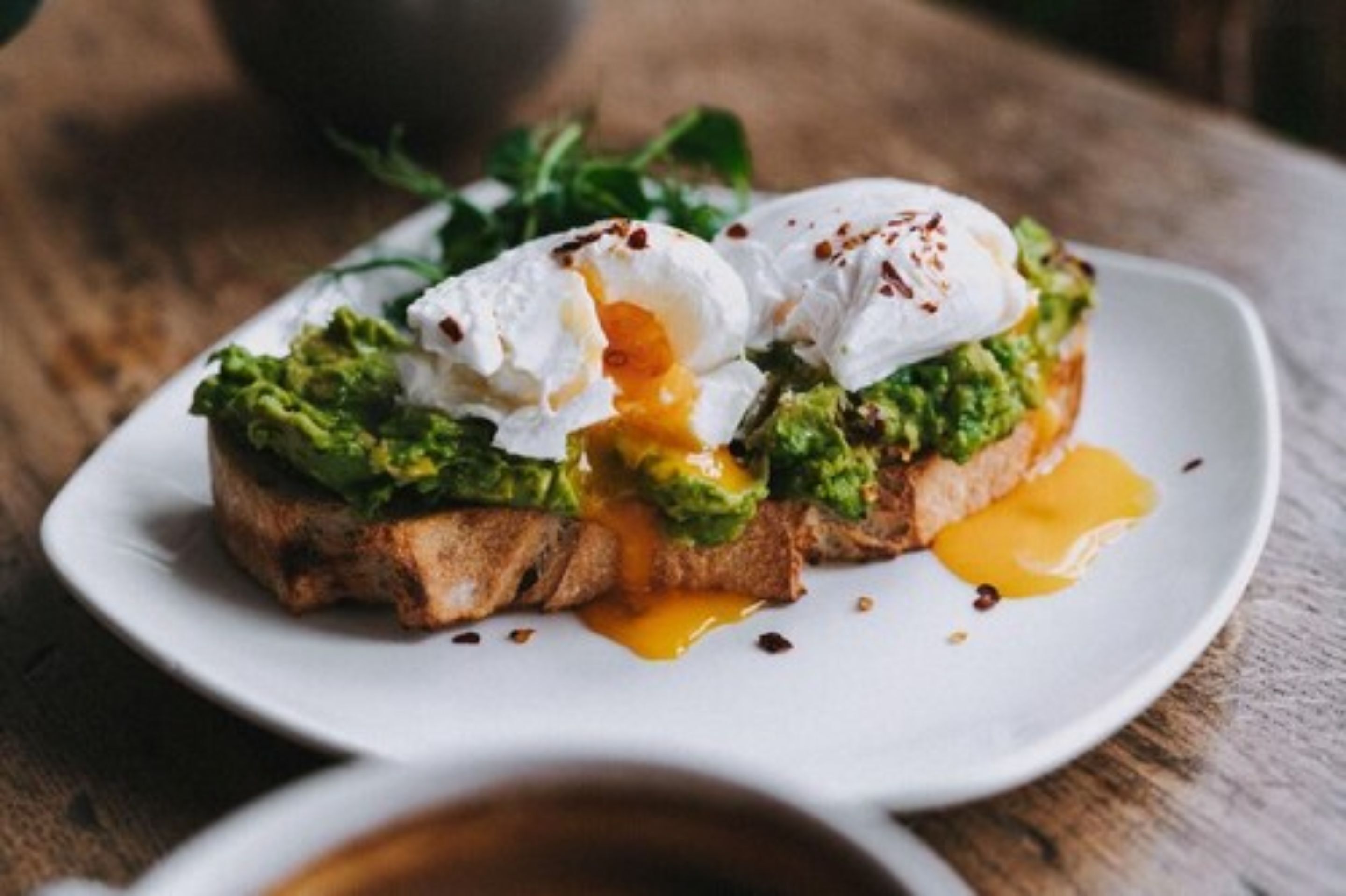 A breakfast dish with avocado, poached egg, and sauce on toast.