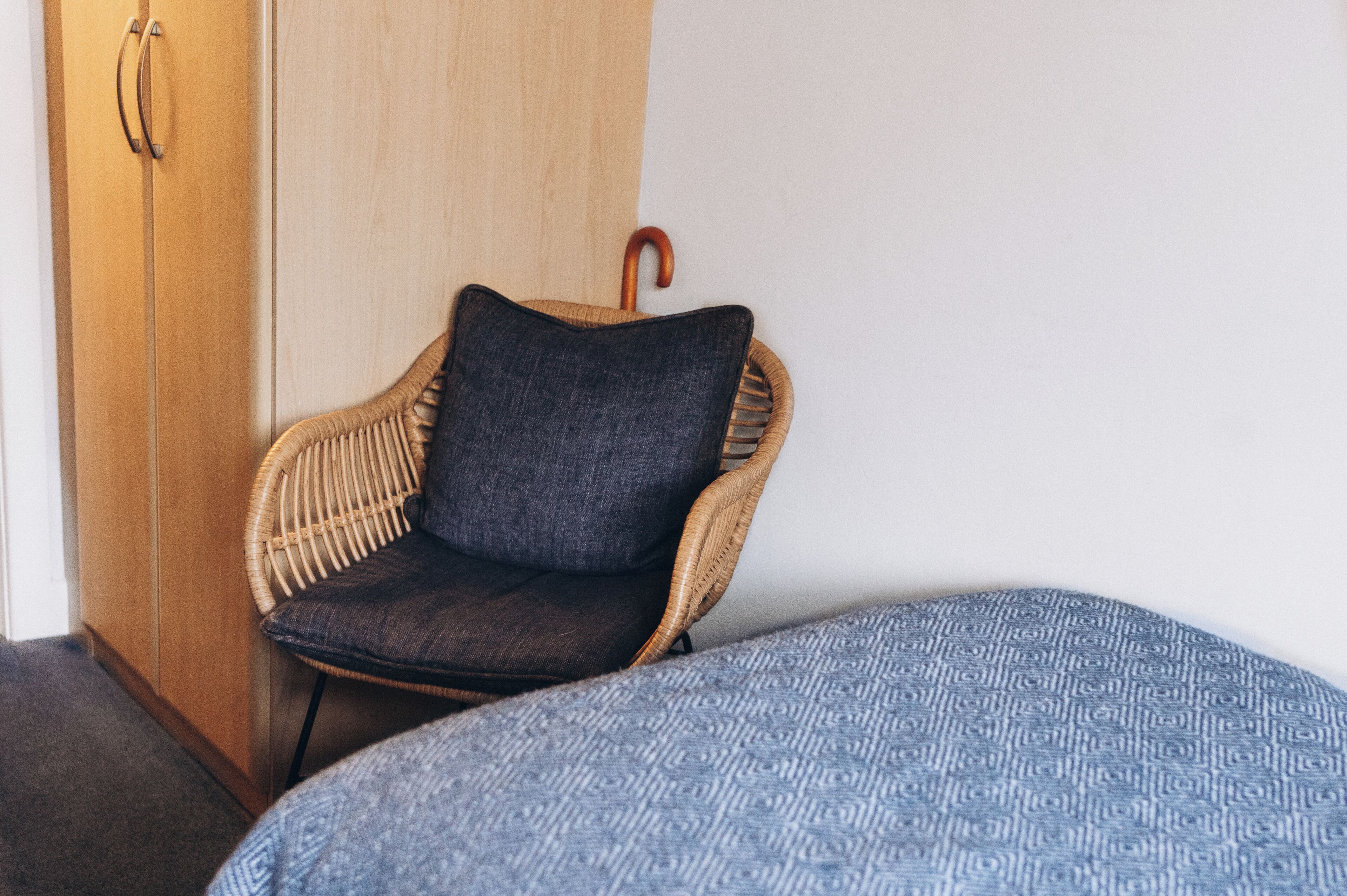 A wicker chair with a dark cushion and a blue patterned bed.