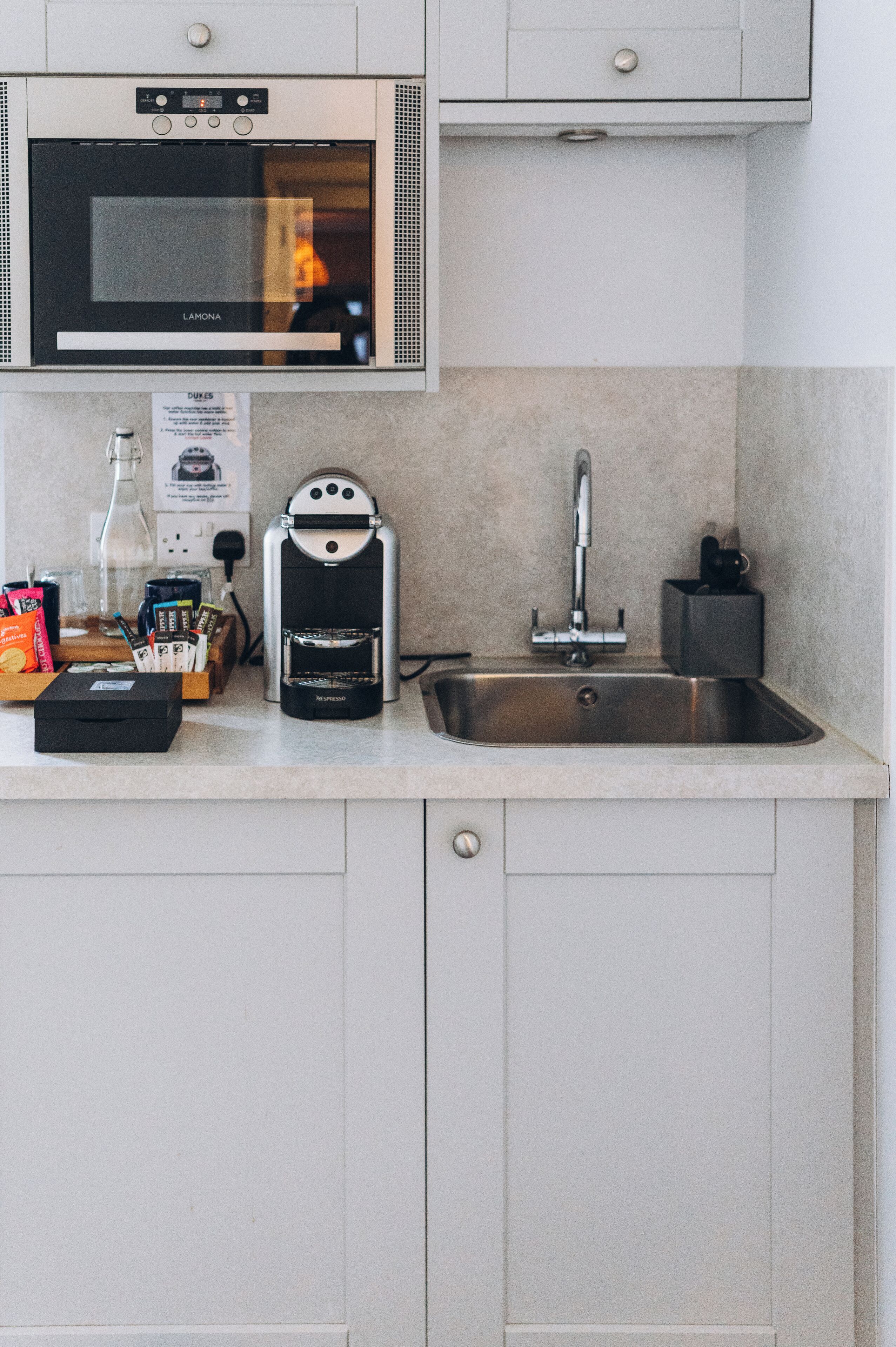 A kitchen with a built-in oven, a coffee maker, a sink, and a countertop with various items.