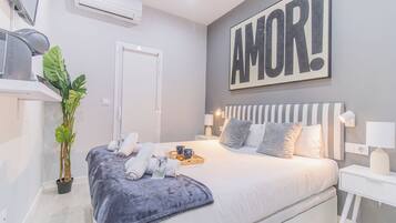 Une chambre moderne avec un grand lit, une plante en pot et un mur sur lequel est écrit le mot « AMOR ! ».