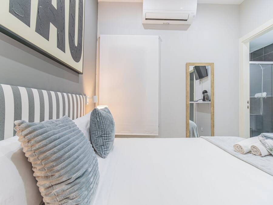 Una habitación de hotel moderna con cama, un espejo grande, un armario y un equipo de aire acondicionado.