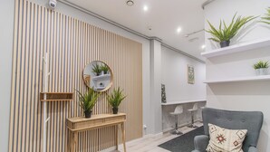 Un salon moderne avec un canapé gris, une console en bois agrémentée de plantes, un miroir rond et un mur à rayures.