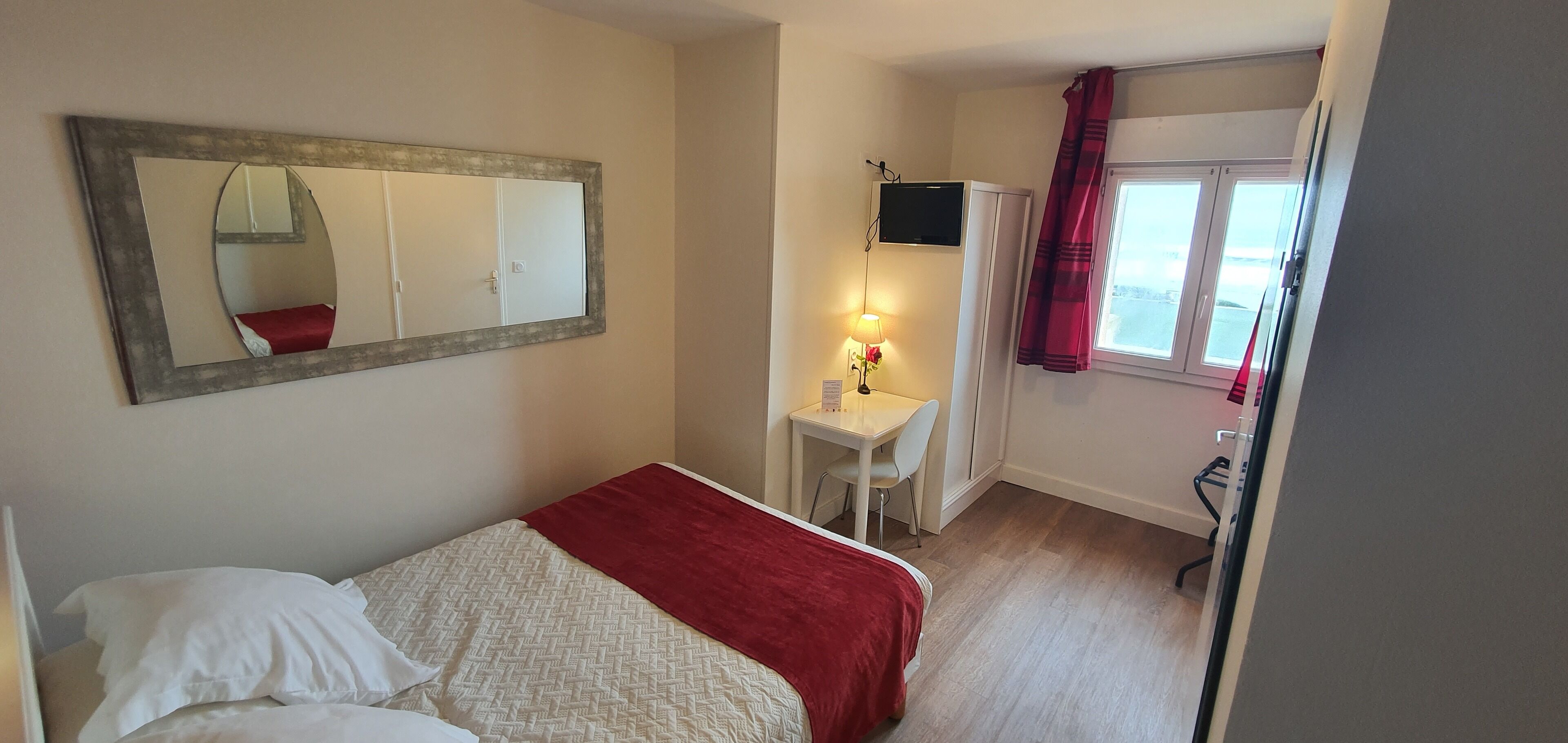 Un dormitorio con cama, una mesita de noche con lámpara, un espejo y una ventana con cortinas.