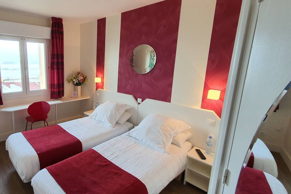 Habitación de hotel con dos camas, un escritorio, una silla, un espejo y una ventana con cortinas.