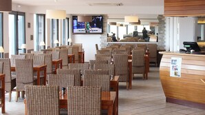 Un hall de hotel con sillas de mimbre, un mostrador de recepción, una pantalla de televisión y una zona de bar.