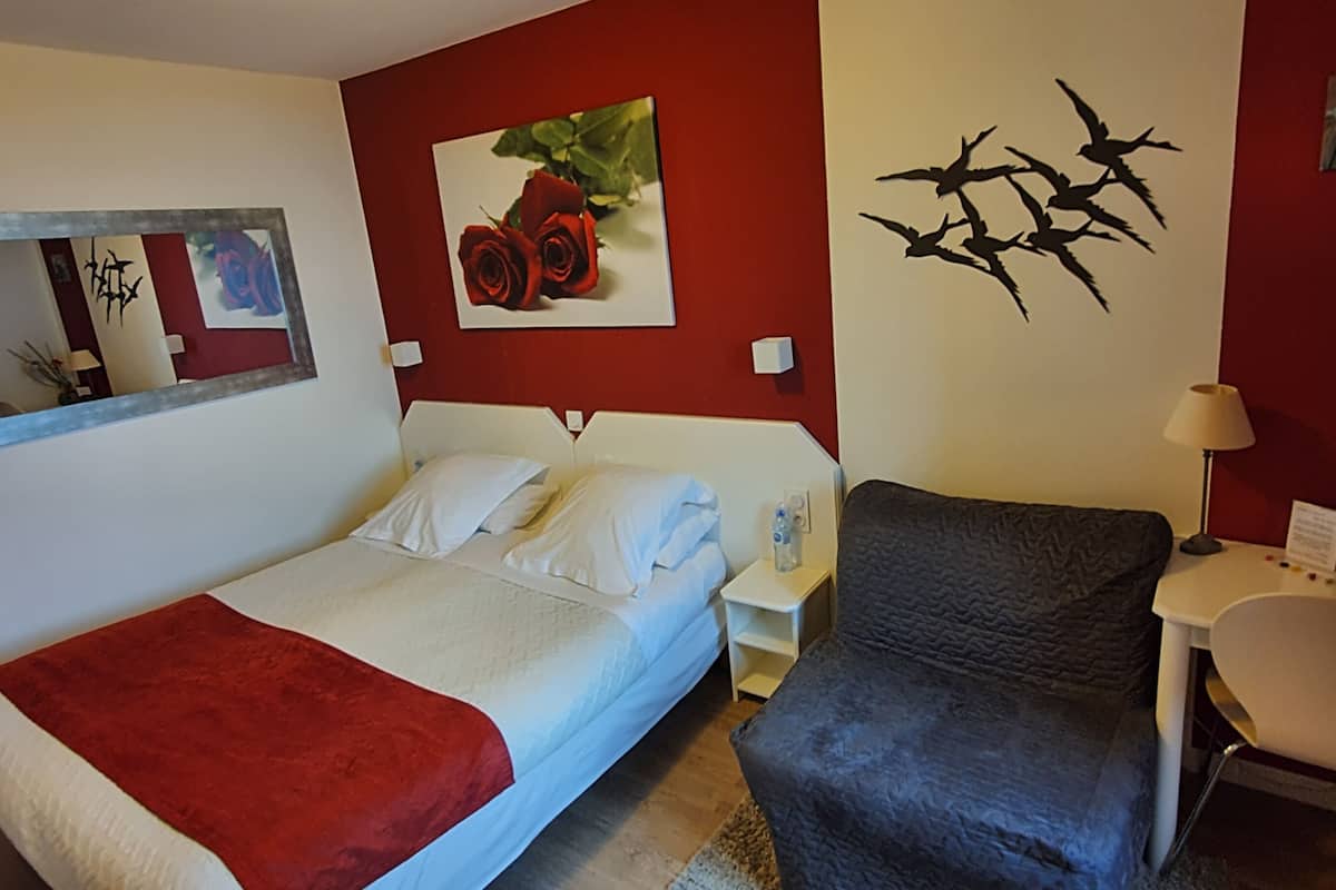 Una habitación de hotel con una cama, una silla, un escritorio, un espejo y obras de arte en las paredes.