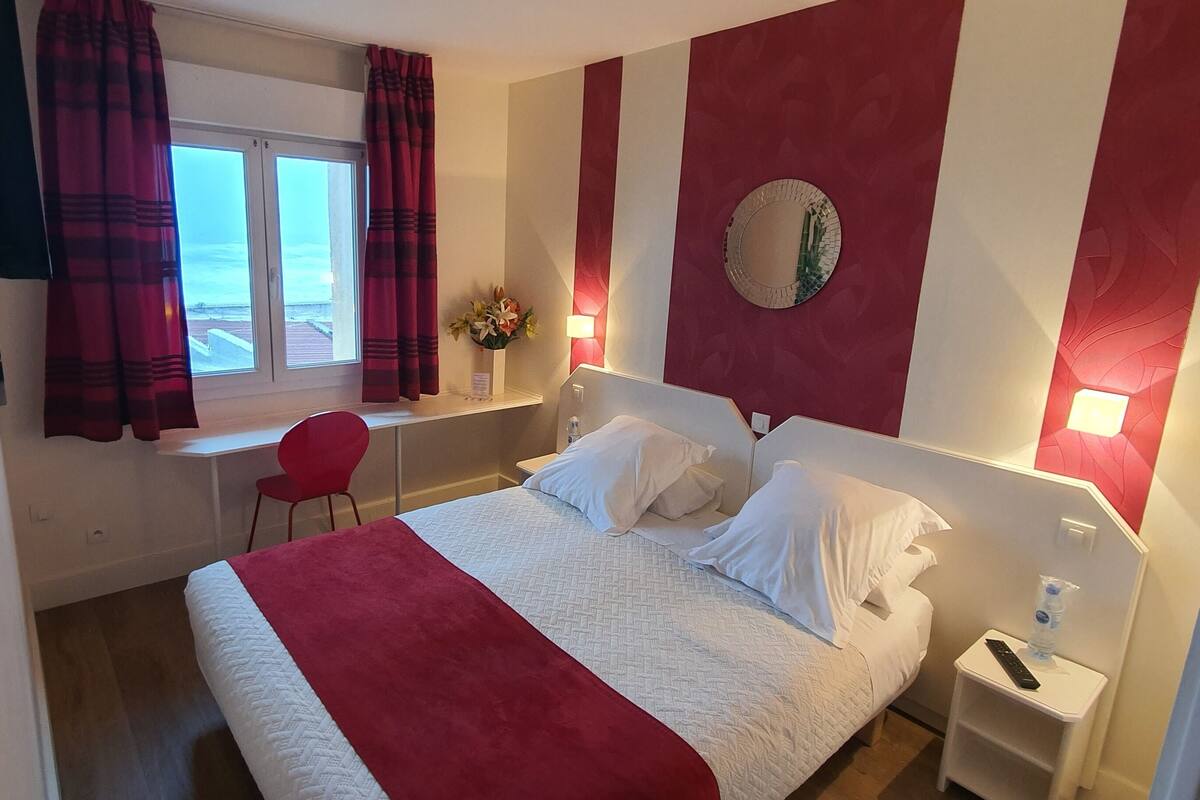 Una habitación de hotel con cama, escritorio, silla, mesita de noche y ventana con cortinas.