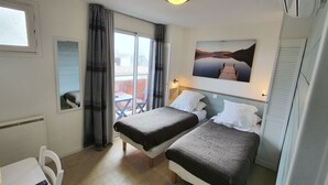 Habitación de hotel con dos camas, una ventana, un cuadro y un balcón con vistas.