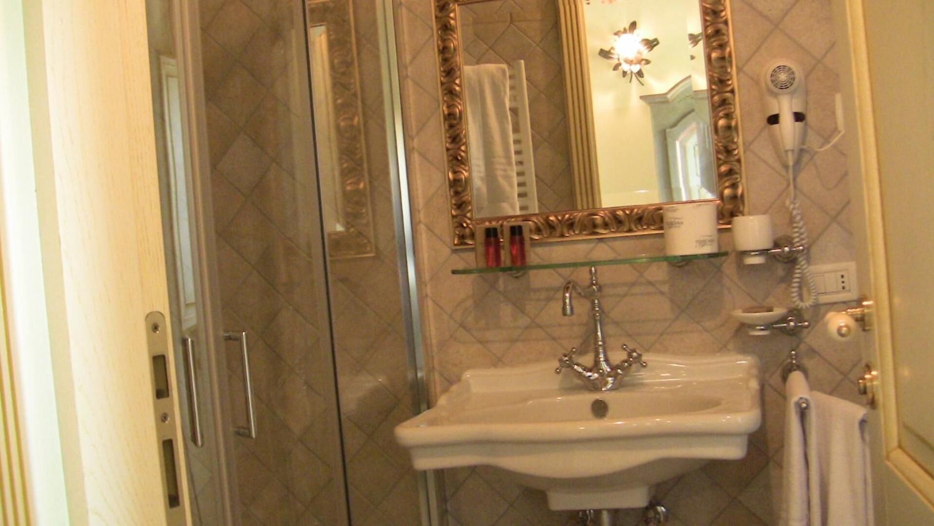 A bathroom with a glass shelf holding toiletries, a sink with a faucet, and a mirror with an ornate frame.