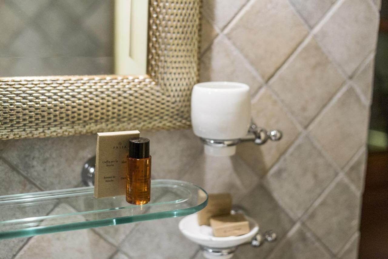 Um banheiro com prateleira de vidro contendo uma garrafa e um sabonete, vaso sanitário branco e parede com textura.