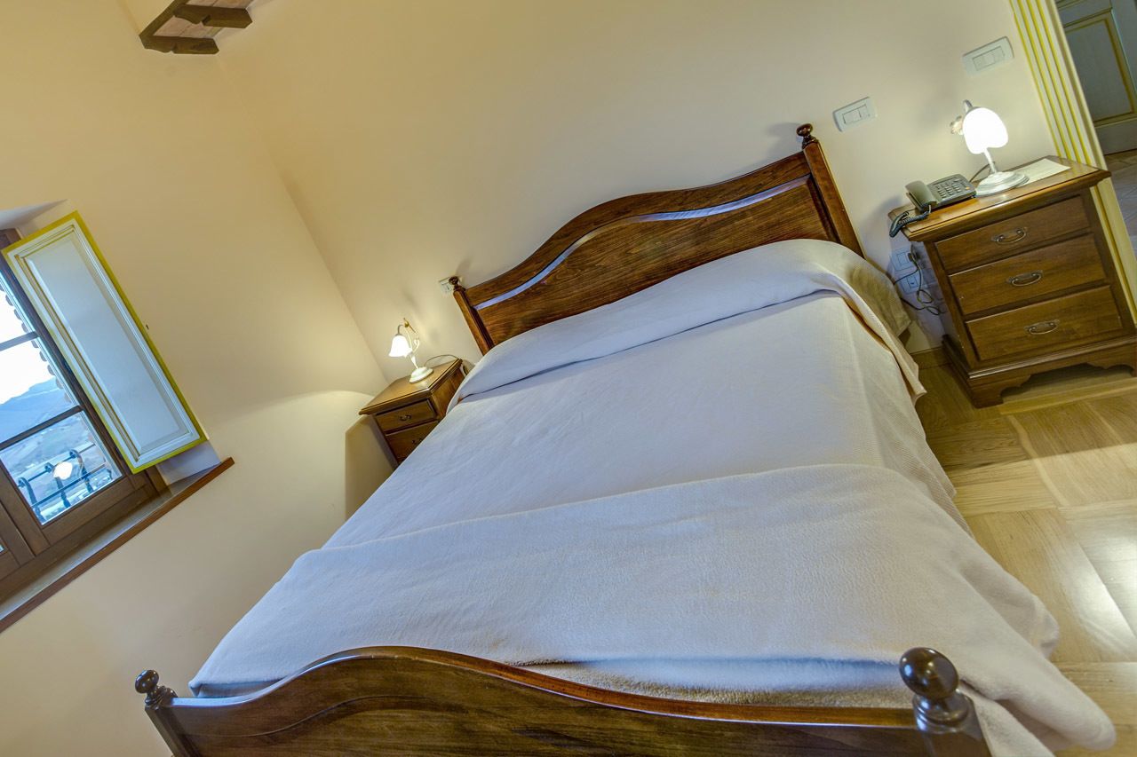 Un lit bien fait, avec une tête de lit en bois, une table de chevet avec une lampe et un miroir accroché au mur.