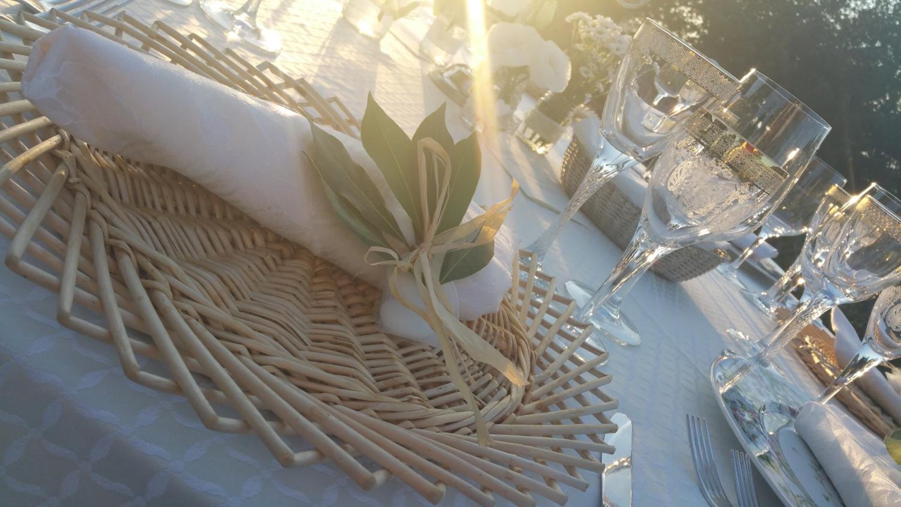 Une table dressée pour un repas, avec un set de table en fibres tressées, une serviette pliée et de la verrerie transparente.