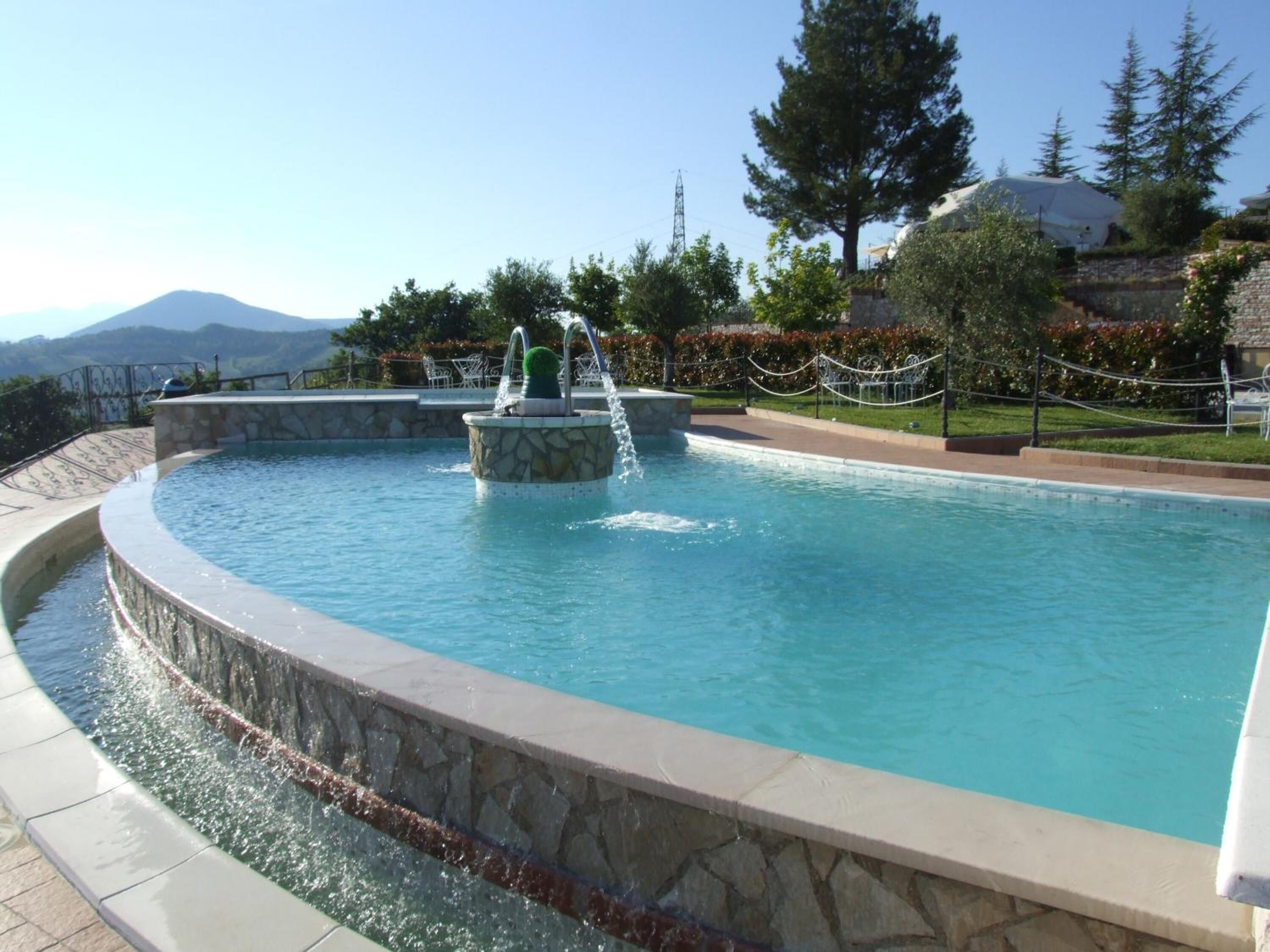 Una piscina circular con una fuente central, rodeada de muros de piedra y un sendero de piedra.