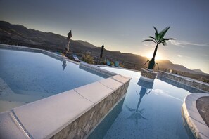 A pool with a clear view of mountains in the background, a palm tree, and a statue. - La Castellaia Resort (Fabriano)