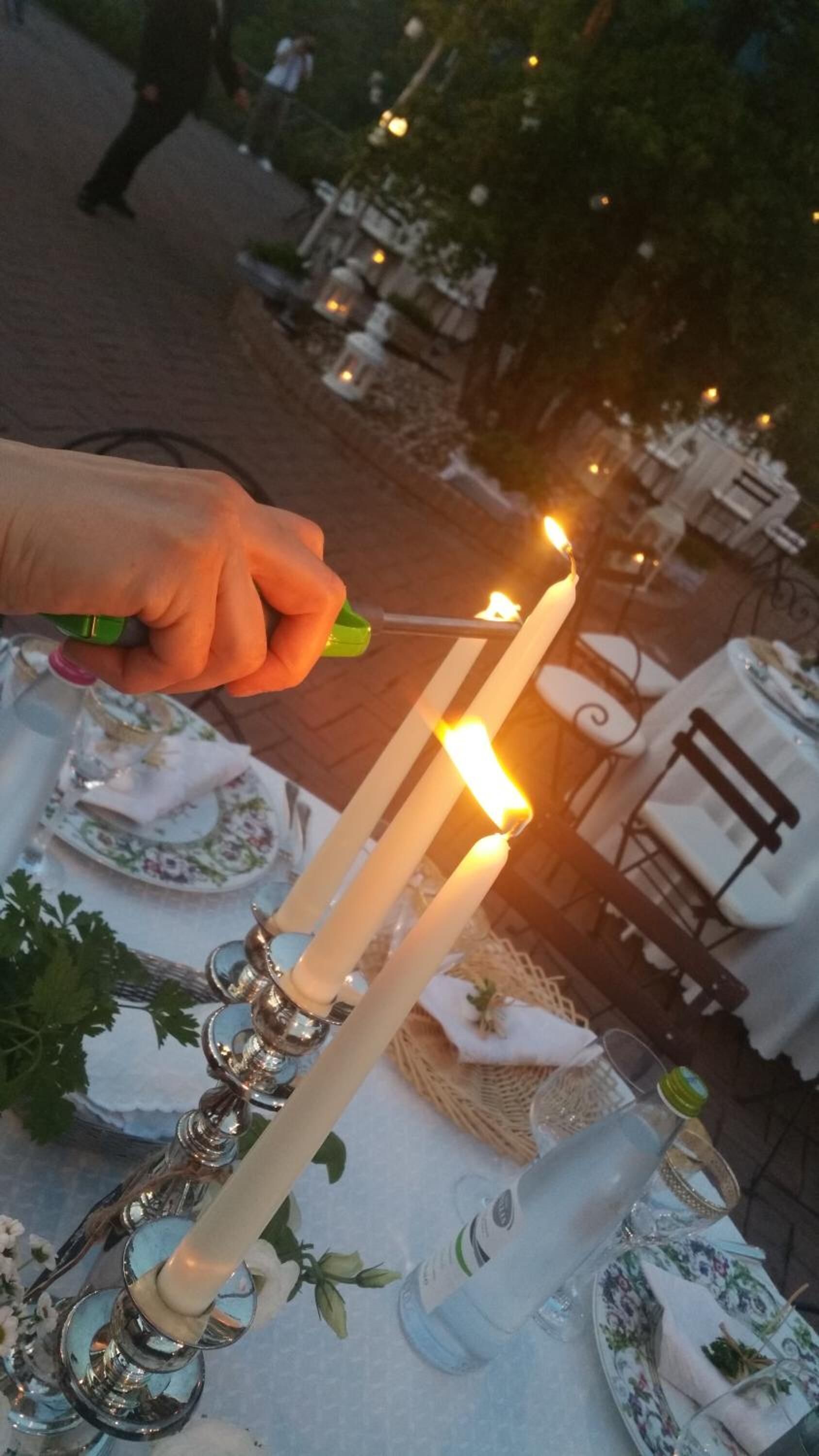 Una mano encendiendo una vela sobre una mesa con un centro de mesa floral y un candelabro.