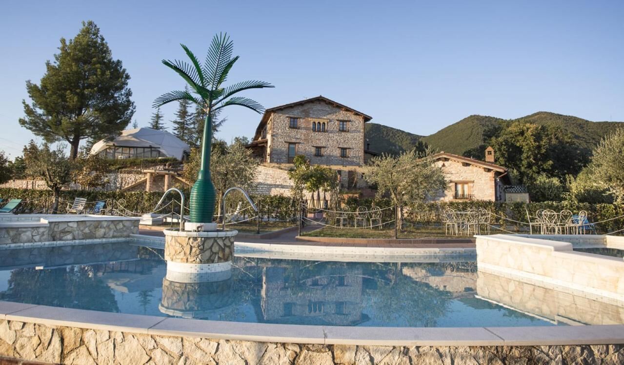 A pool area with stone walls and a palm tree, surrounded by a stone pathway and lounge chairs.