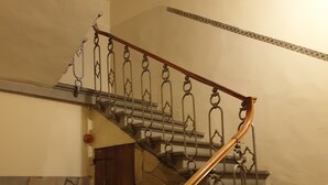A staircase with a wooden handrail and metal balusters, leading to a door with a stone wall and patterned carpet. - Soggiorno Annamaria (Florence)