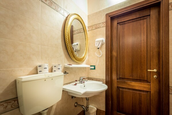 A bathroom with a toilet, sink, mirror, and a wooden door. - Soggiorno Annamaria (Florence)
