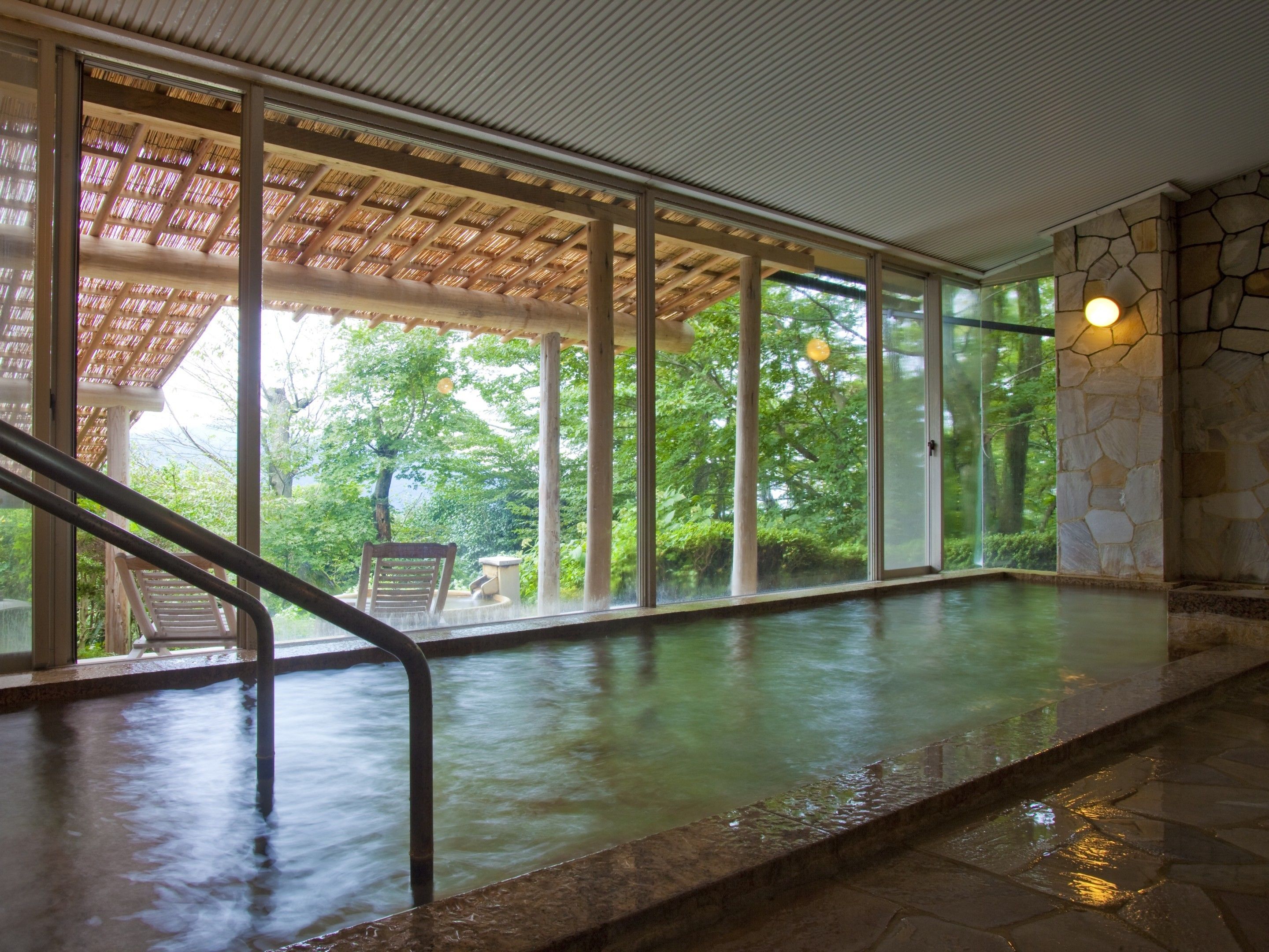 A spa pool with a stone wall, wooden deck, and a view of greenery.