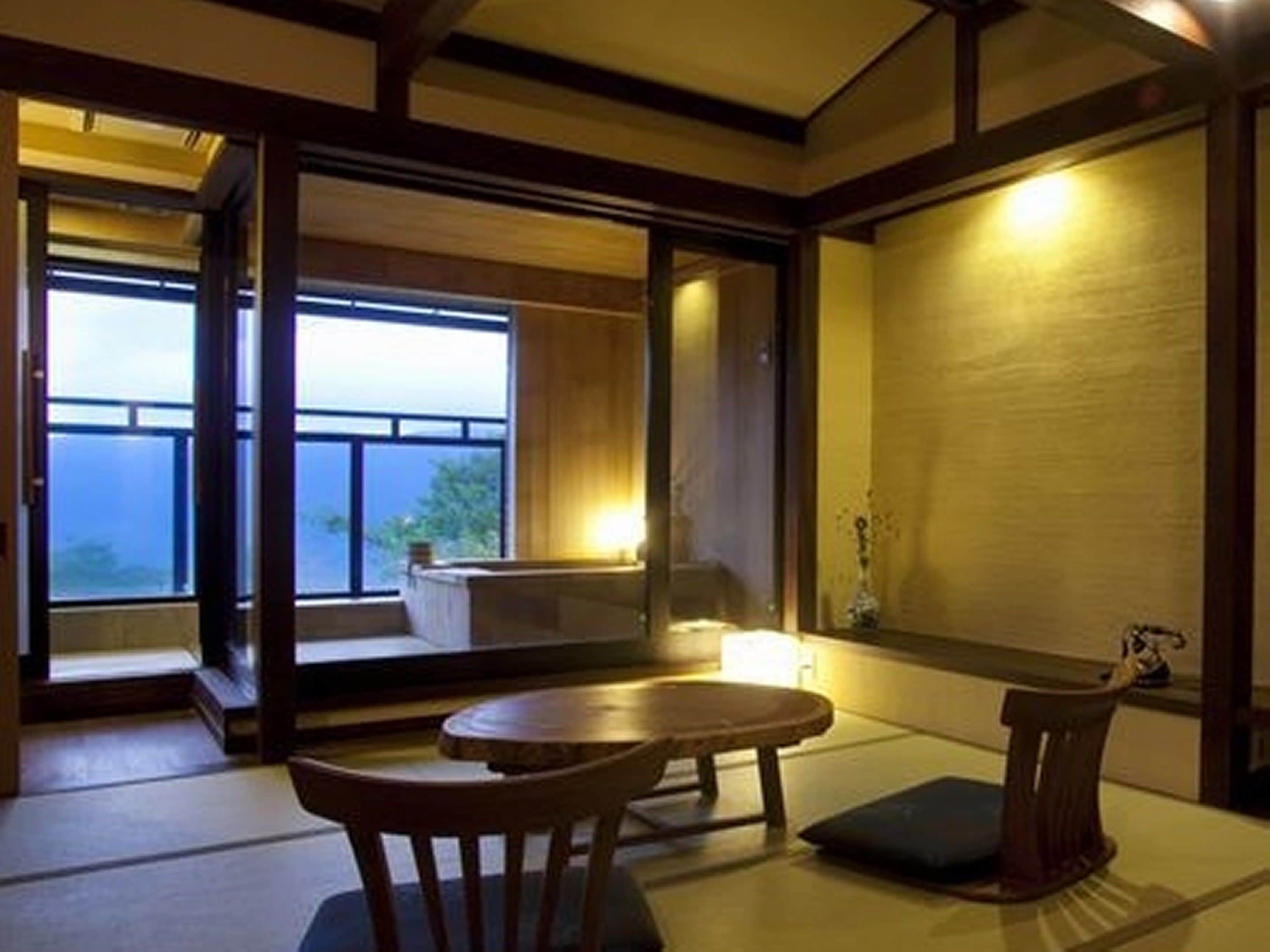 Een traditionele Japanse kamer met tatami vloeren, een lage tafel met kussen en uitzicht op de zee door grote ramen.