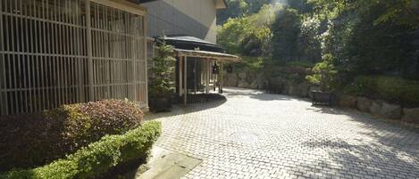 Il s’agit d’un bâtiment traditionnel japonais doté d’une cour dallée, d’une entrée couverte et offrant une vue sur un paysage montagneux.