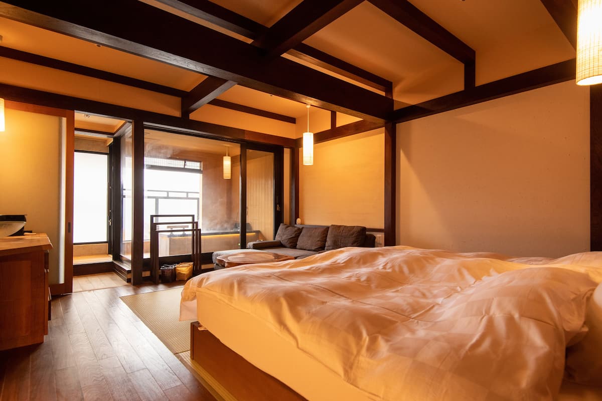 A traditional Japanese-style bedroom with a large bed, wooden beams, and a sliding door leading to a balcony.