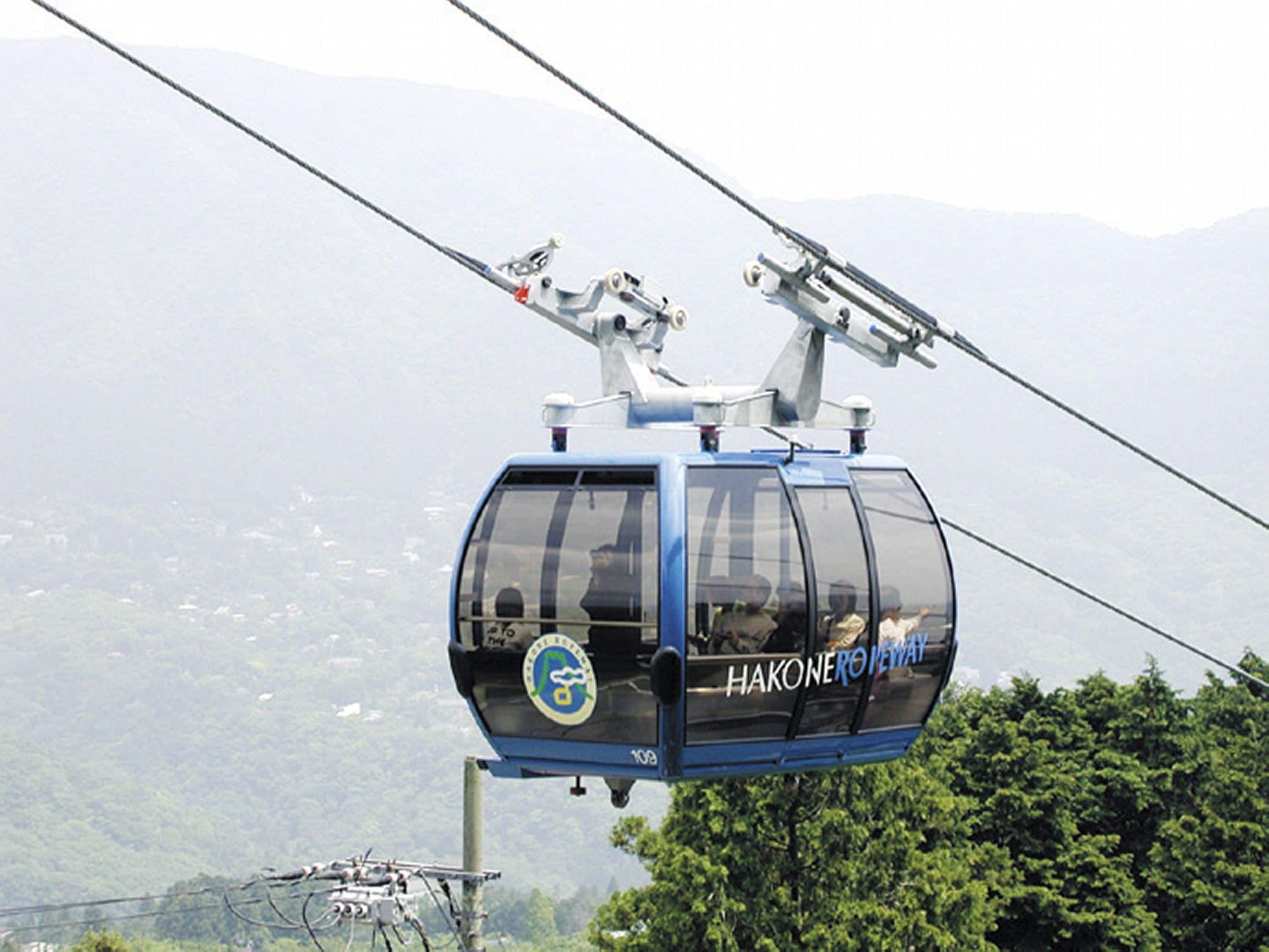 A cable car with "HAKONEROWAY" branding, moving along a cable.