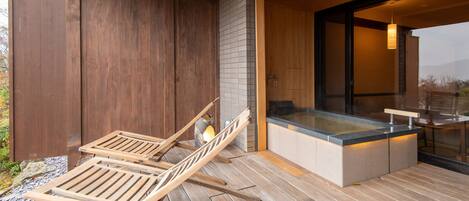 Una terraza de madera con dos sillones de madera, un jacuzzi y un ventanal que da a una habitación.