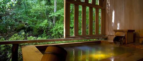 A wooden deck with a glass railing overlooking a forested area.
