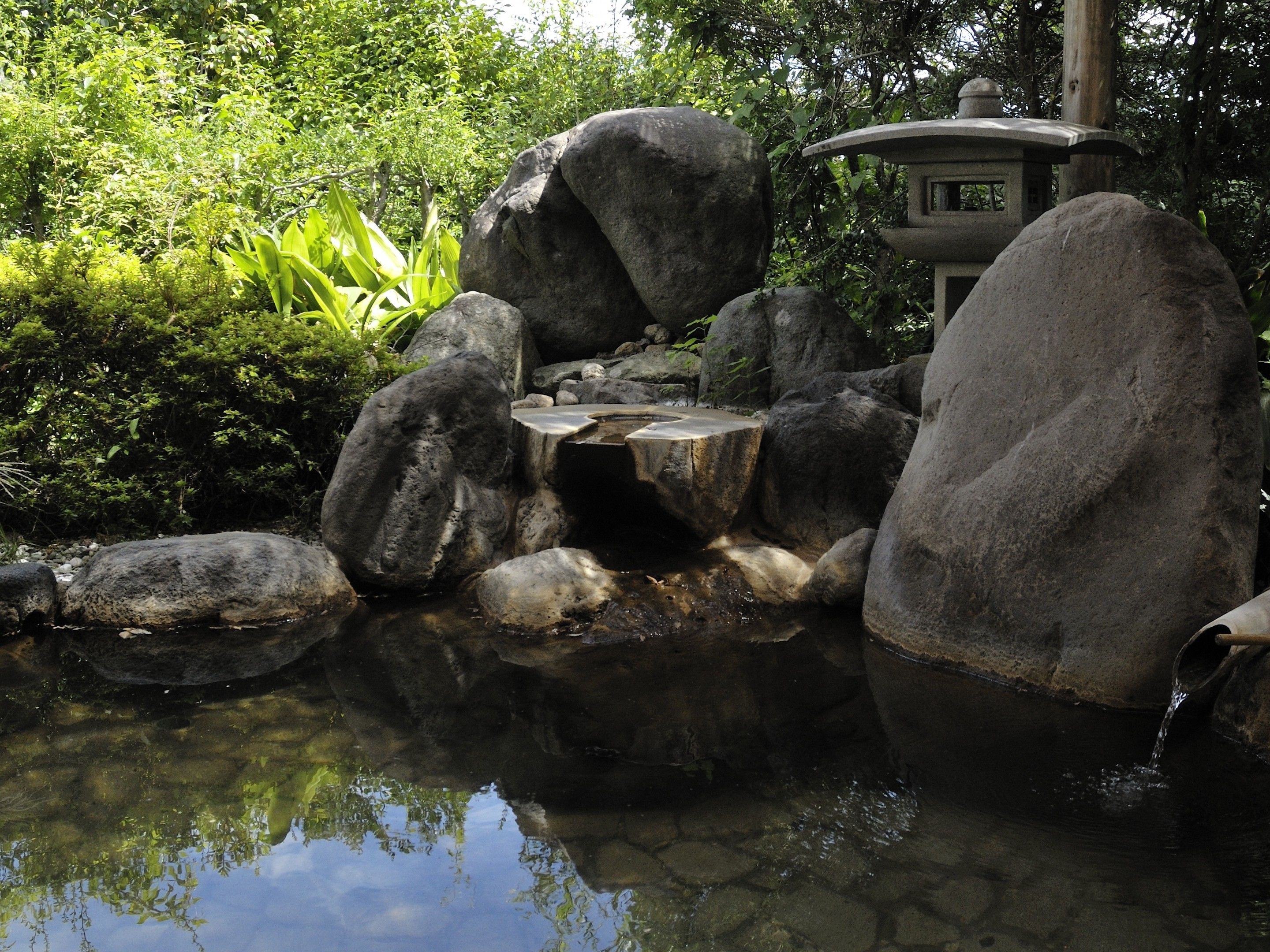 A tranquil garden with a pond, large rocks, and a traditional stone lantern.