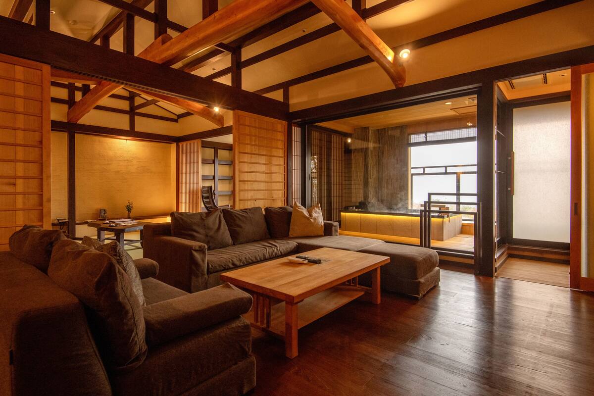 A spacious living area with a wooden ceiling, a sofa set, a wooden coffee table, and a sliding glass door leading to an outdoor balcony.