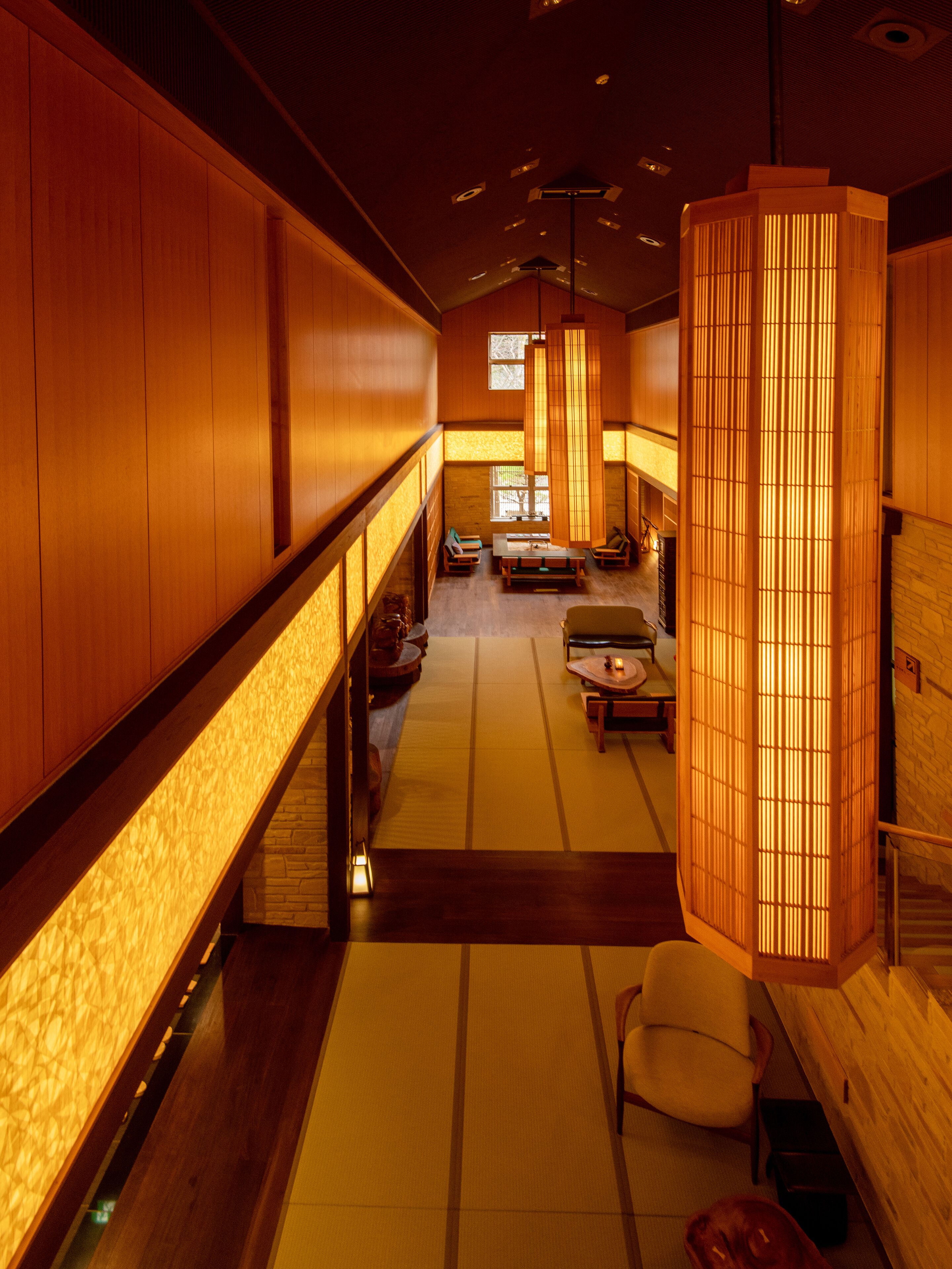 A traditional Japanese-style interior with tatami flooring, low wooden walls, and a central seating area with cushions and a low table.