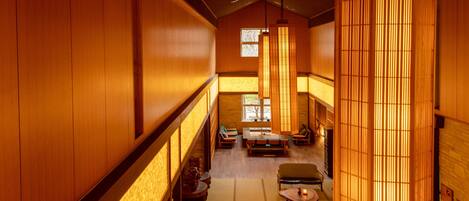 A traditional Japanese-style interior with tatami flooring, low wooden walls, and a central seating area with cushions and a low table.