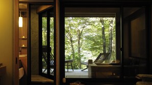 A modern interior with a large glass door leading to an outdoor deck. Inside, there is a wooden bench, a small table, and a basket. - Gora Hanaougi (Hakone)
