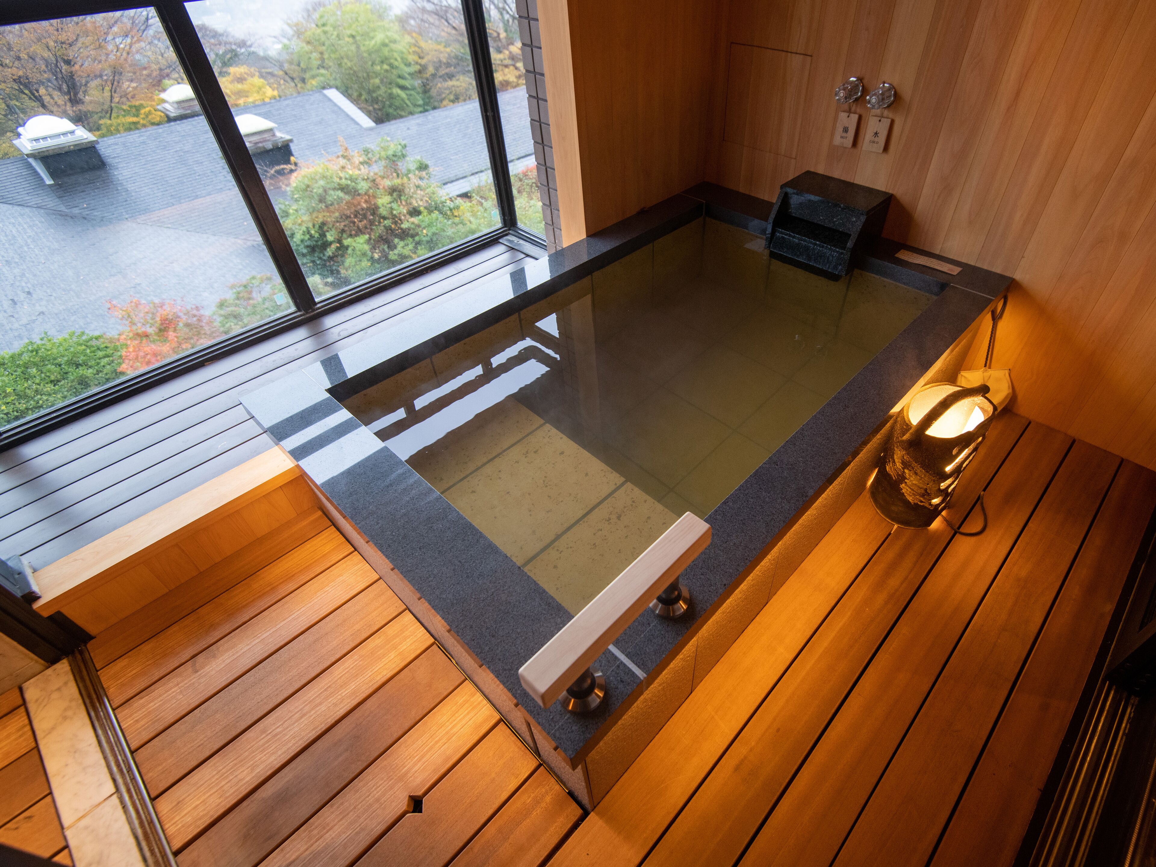 Un baño moderno con bañera de hidromasaje con mampara de vidrio, piso de madera y vistas al exterior.