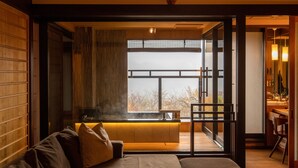 Un interior moderno con un sofá, un banco de madera y vistas a un espacio exterior con banco y árboles a través de una puerta de cristal.