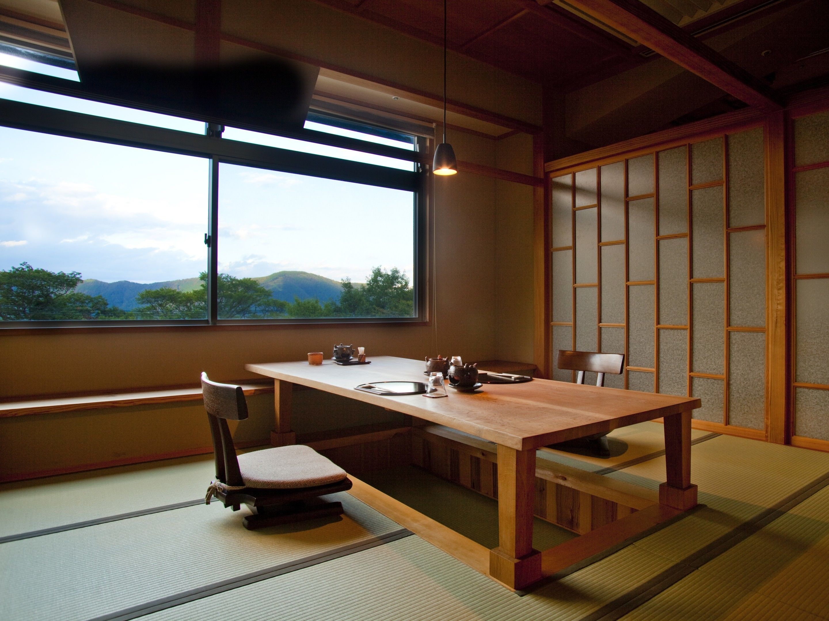 A traditional Japanese room with tatami flooring, a low table, and a view of mountains through a large window.