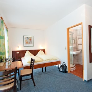 Een slaapkamer met een bed, een bureau met stoelen, een badkamer met een wastafel en douche, en een schilderij aan de muur.